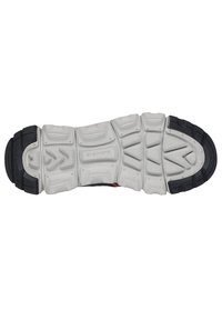 Semelle d'une chaussure de sport avec un motif texturé noir et gris, des rainures profondes pour l'adhérence, et une marque en relief sur la semelle intermédiaire.