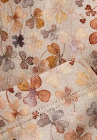 Tkanina w wzór z pastelowymi koniczynami w odcieniach pomarańczowego, żółtego i szarego na strukturalnym, jasnobeżowym tle.