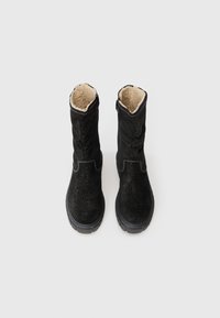Botas de tornozelo em camurça preta com um leve brilho, apresentando um forro de pele de bezerro bege macio, solas de borracha e costura em contraste.