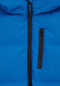 Chaqueta azul acolchada con cremallera frontal y un bolsillo en el pecho con cremallera negra. La tela es suave y tiene un ligero brillo.