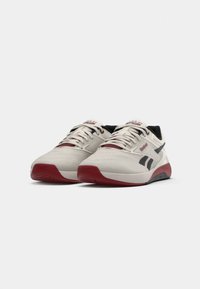 Hvite sportssko med røde detaljer og svarte aksenter. Har tekstilmateriale og snøring, med en buet såle og logo på siden.