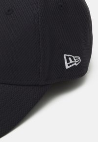 Black cap with a textured fabric, featuring a curved brim and a white embroidered logo on the side. Subtle, modern design elements.