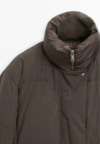 Brun pufferjakke med en høj, polstret krave, lynlås og trykknapdetaljer. Stoffet har en glat tekstur med en subtil glans.