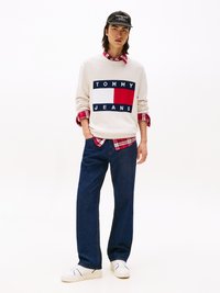 Kreem-sinine sviiter, millel on mereväe sinise ja punase värvi "TOMMY JEANS" logo, kantud punase ruudulise särgiga, koos tume denim teksade ja valgete sneakeritega.