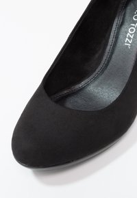 Chaussure femme plate en daim noir avec bout arrondi et semelle intérieure grise visible affichant partiellement le texte de la marque sur un fond blanc.