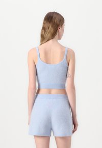 Svetlo modrý pletený crop top a šortky, s jemnou textúrou, rípovanými okrajmi a priliehavým strihom. Zadný pohľad zdôrazňuje jednoduchosť.