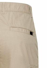 Beige pants section showing a back slit pocket with a small black label on the right side below the waistband.