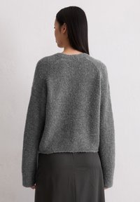 Grijze wollen trui met een relaxte pasvorm, voorzien van lange mouwen en een ronde halslijn, gecombineerd met een zwarte leren rok.