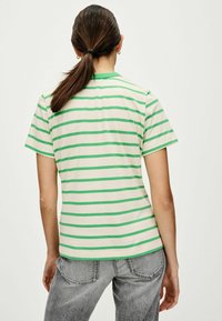Pasiasta koszulka w kolorze off-white i zielonym, z okrągłym dekoltem, krótkimi rękawami, wykonana z miękkiego materiału. Widoczne szare dżinsy poniżej. Minimalistyczny design.