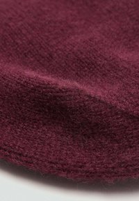 Tessuto di lana bordeaux dalla texture morbida, che presenta un delicato motivo intrecciato e un bordo leggermente curvo. Ideale per cappelli o abbigliamento invernale.