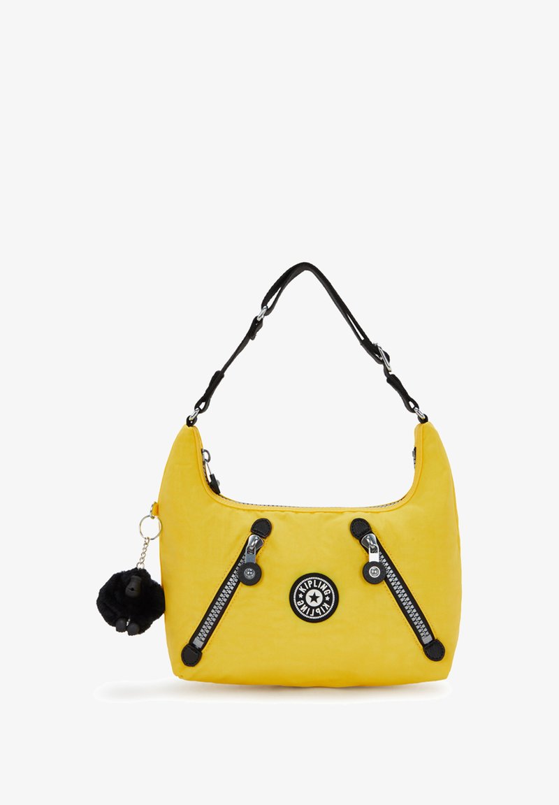 Bolso amarillo con una textura suave, cremalleras y detalles en negro; presenta un logo redondo y un llavero de pom-pom negro desmontable.