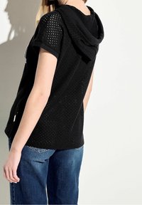 Czarny siatkowy top z kapturem i krótkimi rękawami, z teksturowanym wzorem dzianinowym. Noszony z niebieskimi dżinsami, prezentujący luźny krój i swobodny styl.