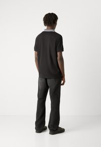 Camisa polo negra con cuello a rayas blancas, combinada con vaqueros oscuros. La camisa tiene mangas cortas y un diseño de corte recto.