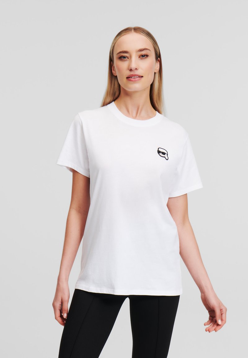 Witte katoenen t-shirt met korte mouwen en een ronde halslijn, met een klein zwart grafisch ontwerp op de borst. Soepele textuur.