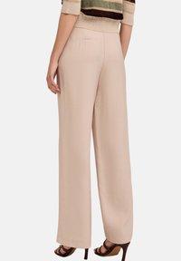 Beige, vloeiende, wijde broek met een gladde textuur en twee achterzakken, gecombineerd met een multi-gestreept top en bruine hakschoenen.