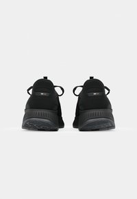 Paire de chaussures de sport noires vues de dos avec des semelles épaisses texturées et des languettes en boucle au talon sur fond blanc.