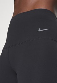 Gros plan d'une personne portant des leggings Nike noirs montrant le haut de la hanche et la ceinture avec le logo Nike swoosh visible.