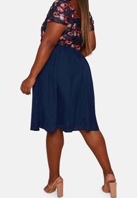 Námořnické šaty s květinovou krajkovou horní částí, krátkými rukávy a splývavou sukní. Mají těsně přiléhající korzet a siluetu do A, doplněné o nahé podpatky.