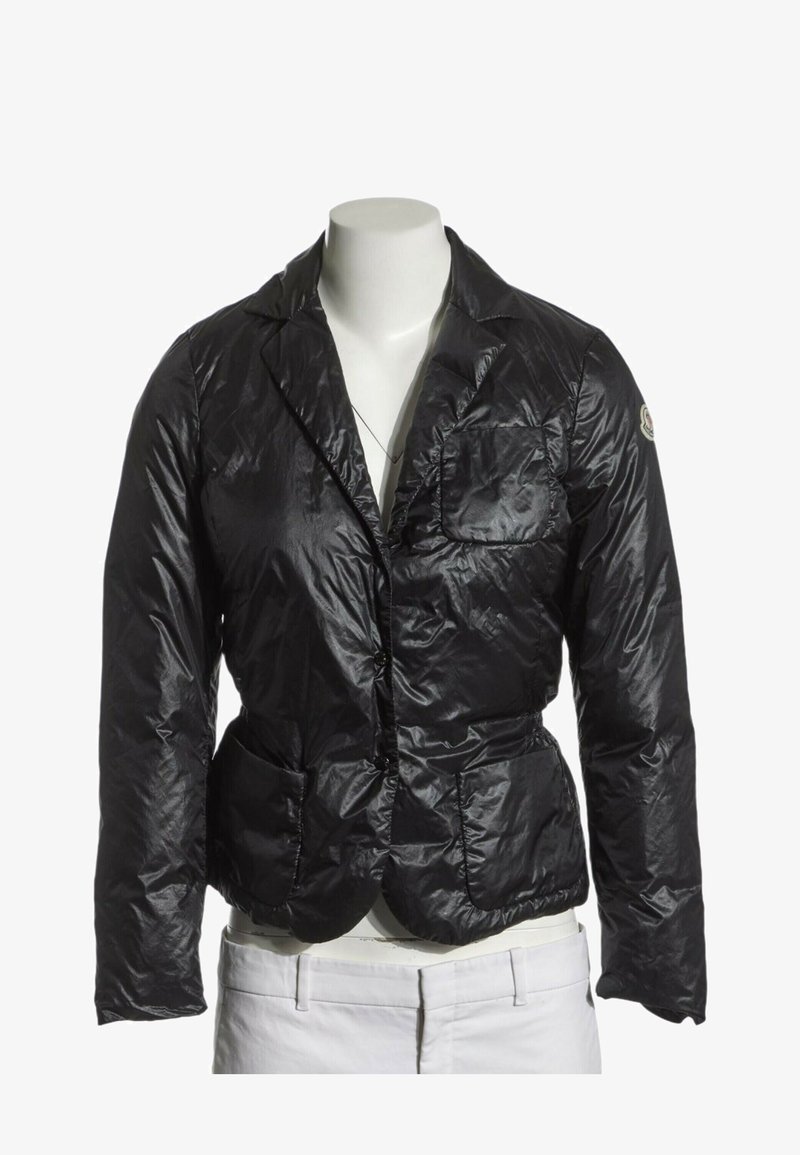 Blazer noir matelassé brillant avec trois poches avant présenté sur un mannequin sans tête portant un pantalon blanc.