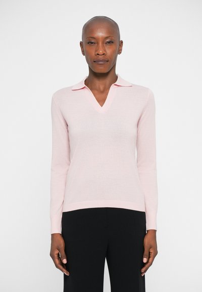 Light pink long-sleeve sweater in a soft material, featuring a V-neck and flat collar design, paired with black trousers.