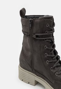 Grey suede ankle boot with lace-up design, side zipper, flat chunky sole, and a loop accent at the top. Textured upper and reinforced stitching.