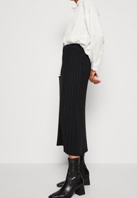 Černá měkká midi sukně s přiléhavým pasem, kombinovaná s bílou košili s knoflíky a černými kotníkovými botami na blokovém podpatku.