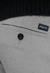 Pantaloni gri cu o textură de țesătură netedă, un singur buzunar pe spate, un nasture negru și o etichetă cu cuvântul "aprel" în alb.