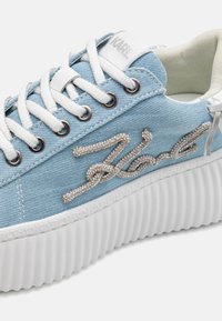 Sneaker in denim azzurro chiaro con suola piatta bianca, accenti in hardware argento e dettagli in strass sul lato. I lacci sono bianchi.