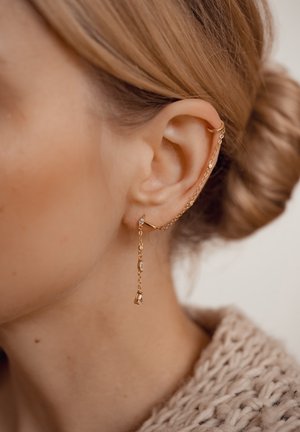 Orecchino in oro con una delicata catena attaccata, decorato con piccole perle e un dettaglio pendente. Indossato sulla parte superiore dell'orecchio, mette in risalto un design minimalista.