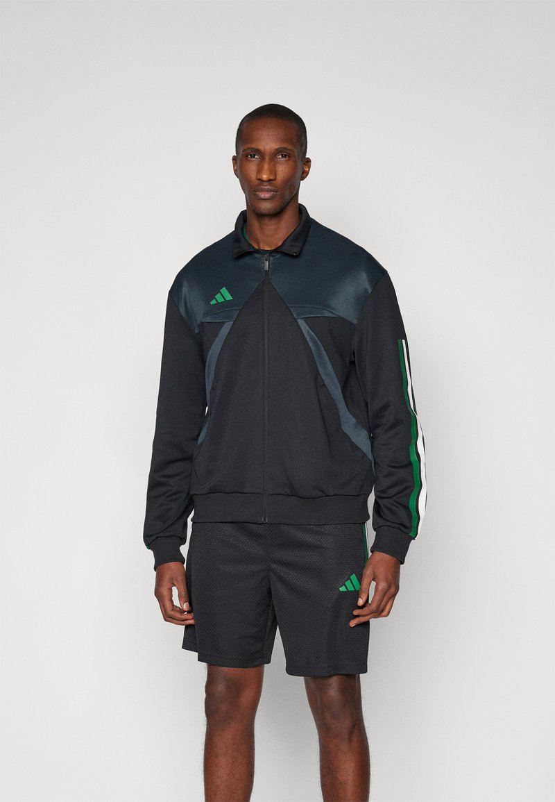 Veste de sport zippée noire avec des rayures vertes et blanches, en matériau texturé et au design épuré ; associée à un short en mesh noir.