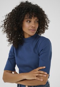 Blå ribbad stickad turtleneck-top med korta ärmar, med en figurnära silhuett och mjuk textur, bärs tillsammans med avslappnade jeans.