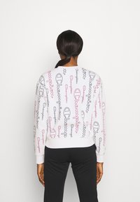 Felpa bianca con diversi loghi "Champion" colorati in nero e rosa. Polsini e orlo a coste; tessuto dalla superficie liscia.
