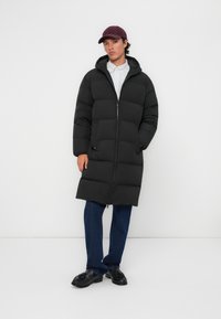 Zwarte pufferjas met een rits aan de voorkant, capuchon en een horizontaal gestikt ontwerp. Draag het over een gestreepte shirt en in combinatie met denim en zwarte schoenen.