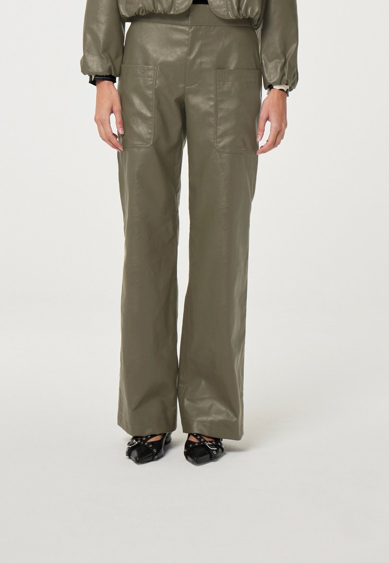 Olijfgroene neplederen wijde broek met twee voorzakken, een soepele textuur en een hoge taille. Zwarte schoenen met decoratieve accenten.