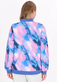 Giacca bomber colorata con un motivo vorticoso in rosa, blu e nero, con colletto e polsini blu solidi. La vista posteriore mostra un orlo elastico.