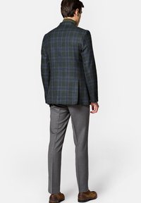 Sprawdzona marynarka w ciemnozielonym kolorze z niebieskimi i czerwonymi akcentami, sparowana z jasnoszarymi spodniami. Materiał wełniany, dopasowany krój z klapami.