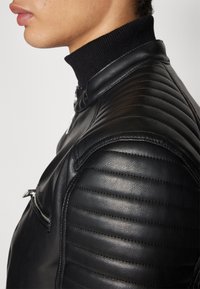 Black leather motorcycle jacket featuring quilted shoulder panels, a high ribbed collar, and silver hardware accents.