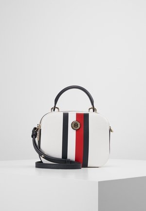 Weiße rechteckige Handtasche mit schwarzen und roten vertikalen Streifen, schwarzem Griff, verstellbarem Schultergurt und rundem goldenen Logo-Emblem.