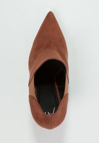 Scarpa in suede marrone a punta con design a intaglio. Presenta un interno nero e accenti marrone chiaro lungo i lati. Suola piatta.