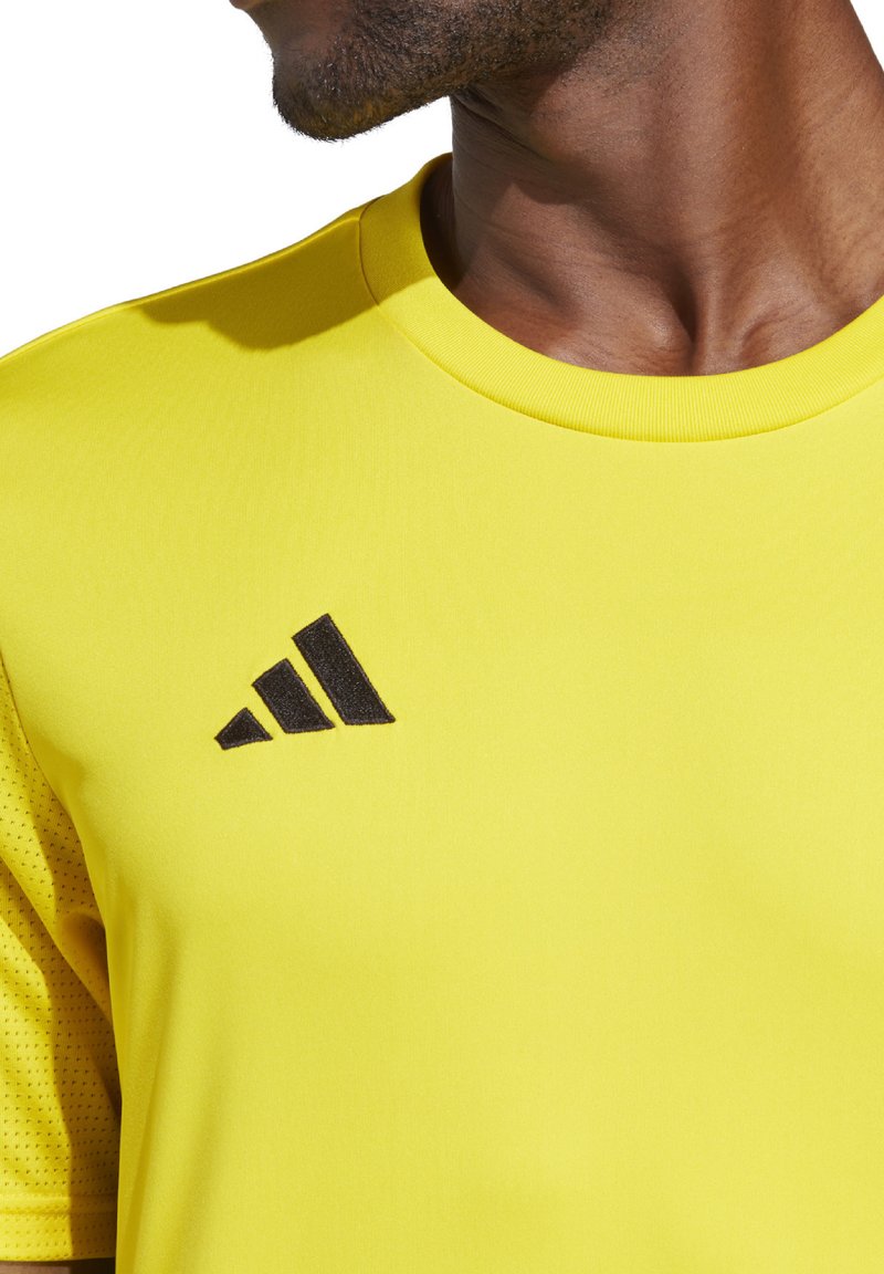 Geel sportshirt met korte mouwen en een ronde halslijn. Zwart Adidas-logo op de linker borst. Glad textuur met ademende mesh-details.