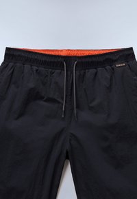 Pantaloncini neri con vita elastica, lacci grigi e fascia interna arancione, con una piccola etichetta rettangolare del marchio sul lato destro.