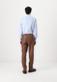 Light blue long-sleeved shirt paired with brown textured trousers. The trousers feature a subtle pattern and back pockets. Black shoes complete the outfit.