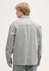 Helles graues Langarmhemd aus strukturiertem Stoff, mit Kragen und knöpfbaren Manschetten, sichtbaren Nähten und einem lässigen Schnitt.