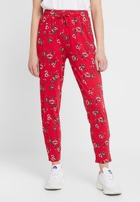 Röda byxor med blommönster, elastiskt midjeband med dragsko, tapered bendesign och mjukt material, kombinerat med vita sneakers.