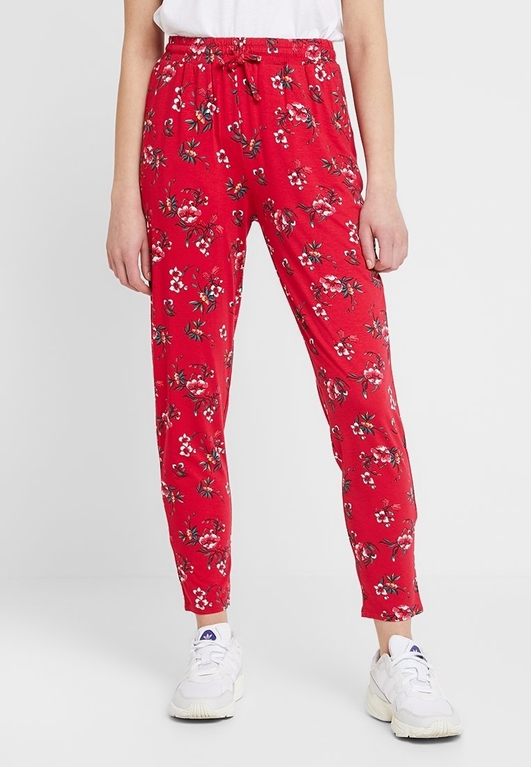 Röda byxor med blommönster, elastiskt midjeband med dragsko, tapered bendesign och mjukt material, kombinerat med vita sneakers.