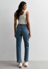 Höga blå denimjeans med rak passform, fem fickor och blekt tvätt, kombinerat med vita sneakers och en åtsittande vit tanktop.