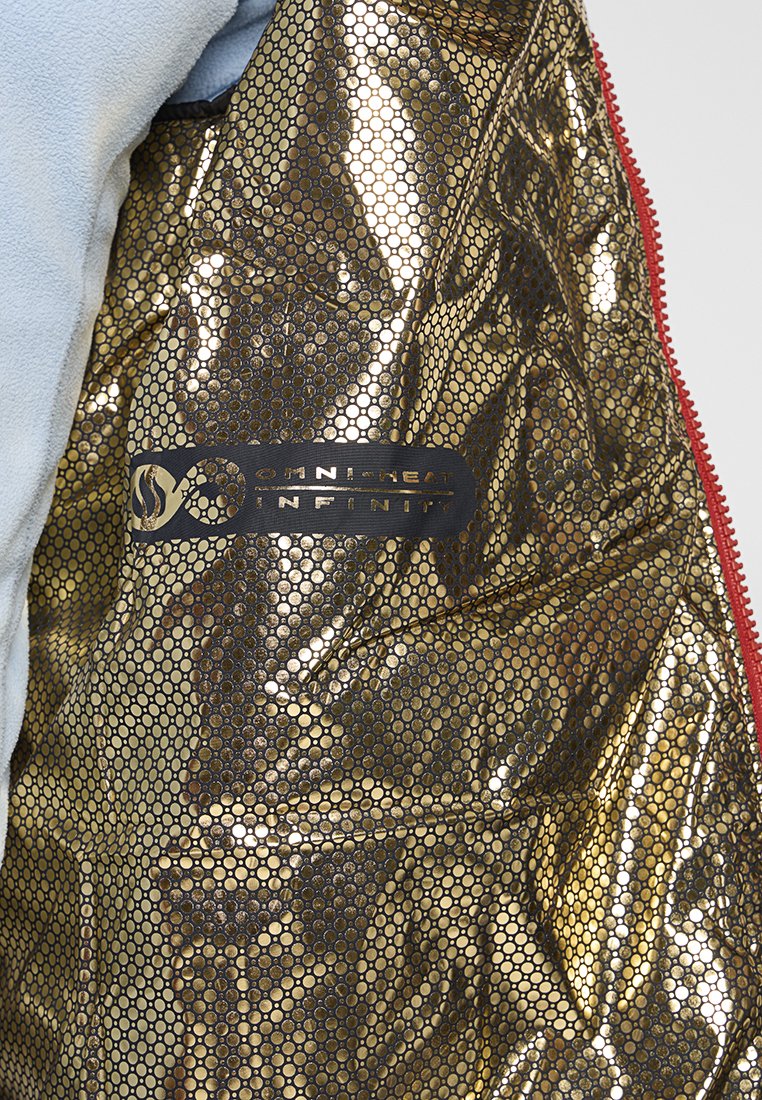 Zbliżenie na złotą podszewkę kurtki w wzór plastra miodu oznaczoną jako "Omni-Heat Infinity" z jasnoniebieskiego materiału i czerwoną krawędzią zamka.