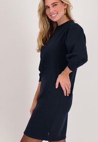 Donkerblauwe jurk met korte mouwen, gemaakt van zacht materiaal, met een losse pasvorm, gathers bij de schouder en een zijrits.