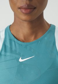Turkooise sporttanktop met gestructureerde patronen, een ronde halslijn en een wit Nike-logo op de voorkant, gemaakt van vochtafvoerende stof.