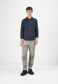 Marineblauw overhemd met knopen van een gestructureerde stof, gecombineerd met lichtgrijze cargobroek met zijzakken en zwarte veterschoenen.